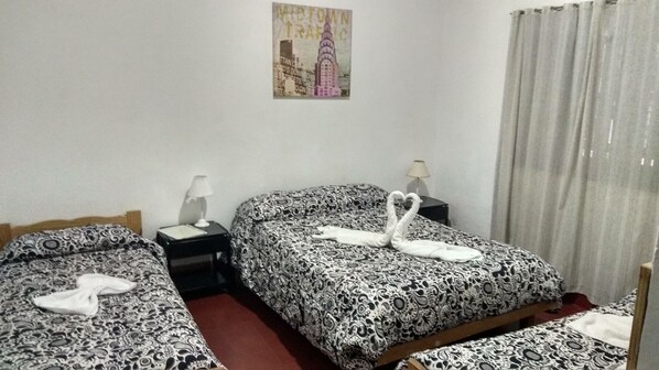 A hotel room with two beds, each with patterned bedding and a decorative swan. There is a nightstand with a lamp between the beds, and a painting on the wall above the beds. - Hotel Colonial (Merlo)