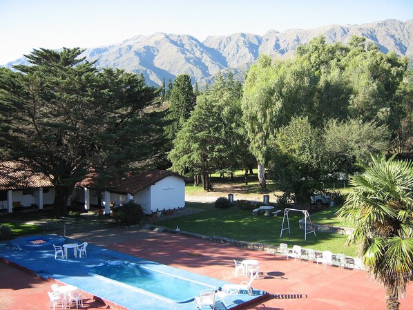 A pool area with lounge chairs and a small building, surrounded by trees and mountains in the background. - Hotel Colonial (Merlo)