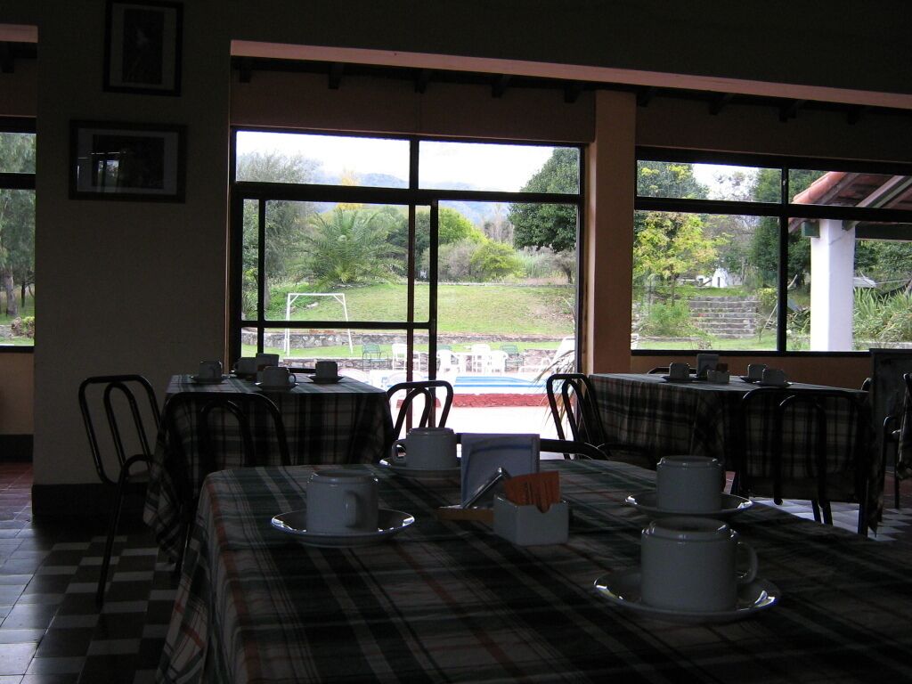 Un comedor con mesas dispuestas para el desayuno, amplias ventanas que dan a un jardín y un edificio exterior.