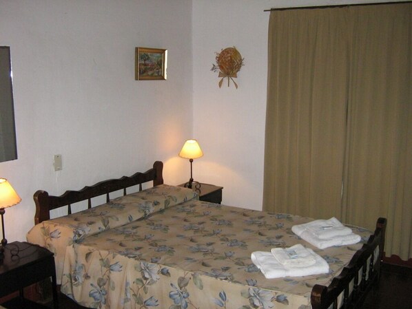 A double bed with floral bedding, two bedside lamps, a small framed picture, and a decorative wall hanging. - Hotel Colonial (Merlo)