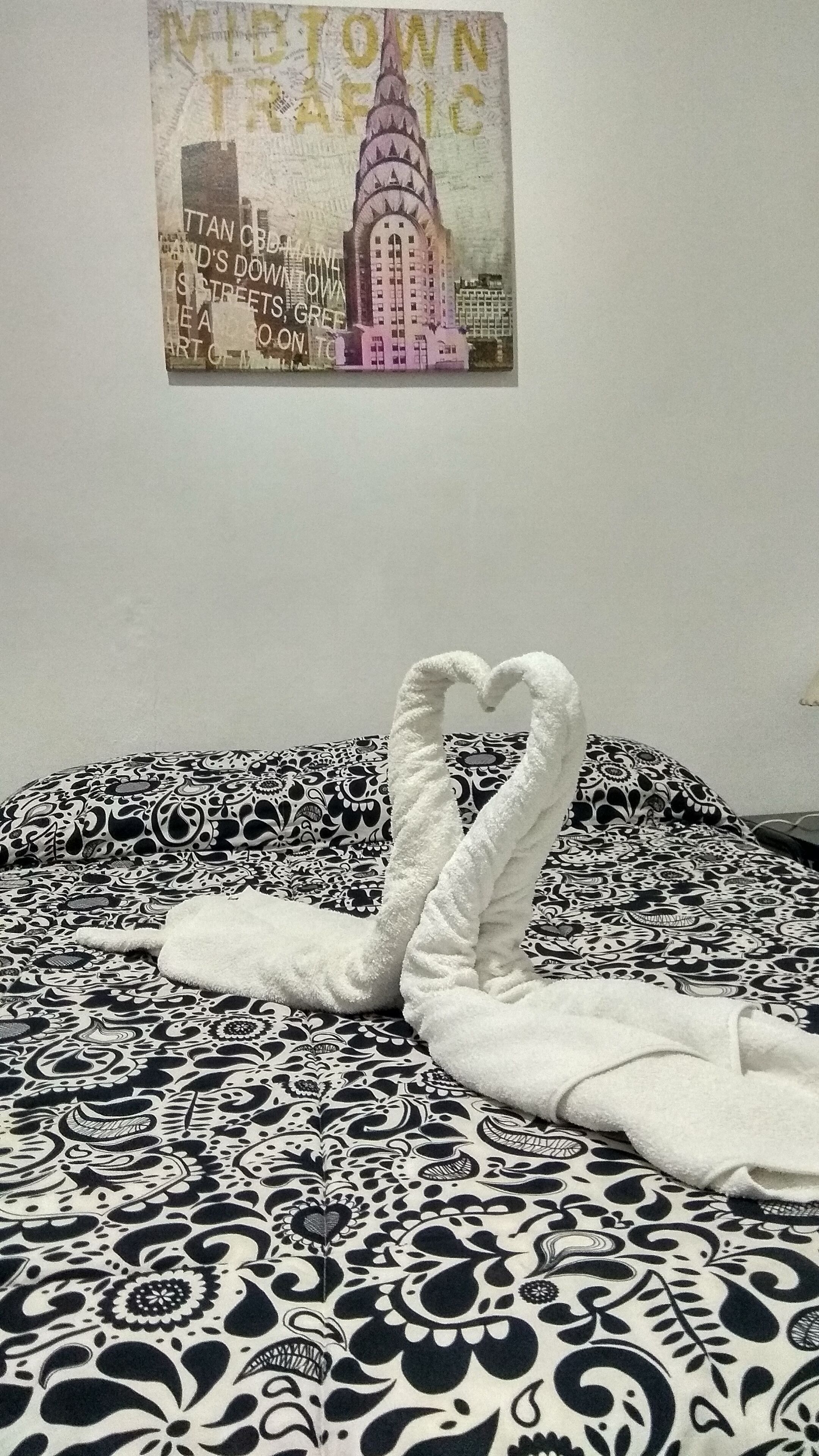 A bed with a black and white patterned bedspread and a towel arranged in a heart shape.