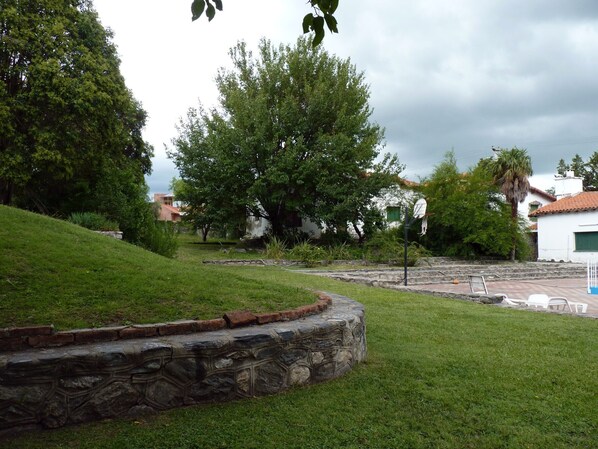 A grassy area with a stone wall, a basketball hoop, and a palm tree. - Hotel Colonial (Merlo)