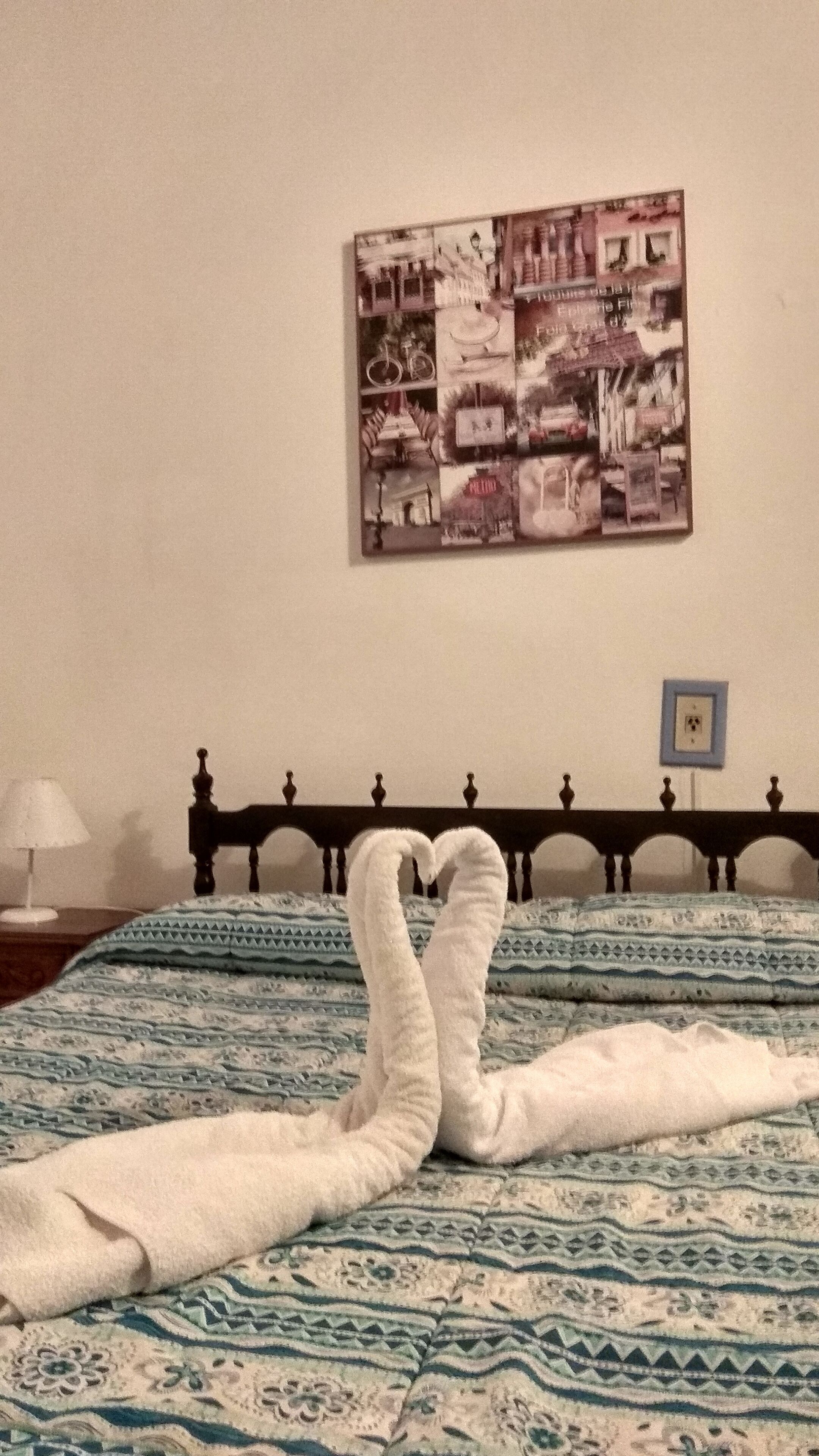 Una cama con colcha azul y blanca estampada, un cabecero con un pequeño marco de fotos y una obra de arte en la pared que muestra diferentes escenas.