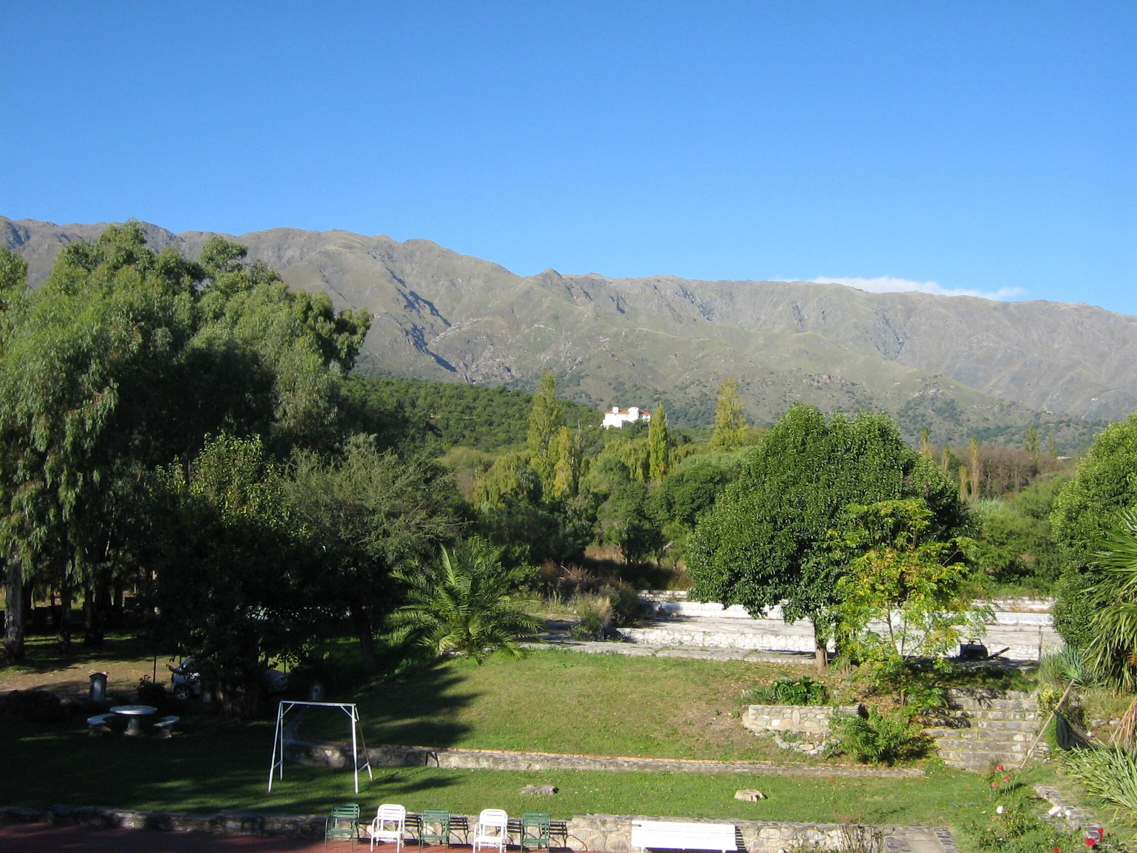 A park with green trees, a white building, and mountains in the background.