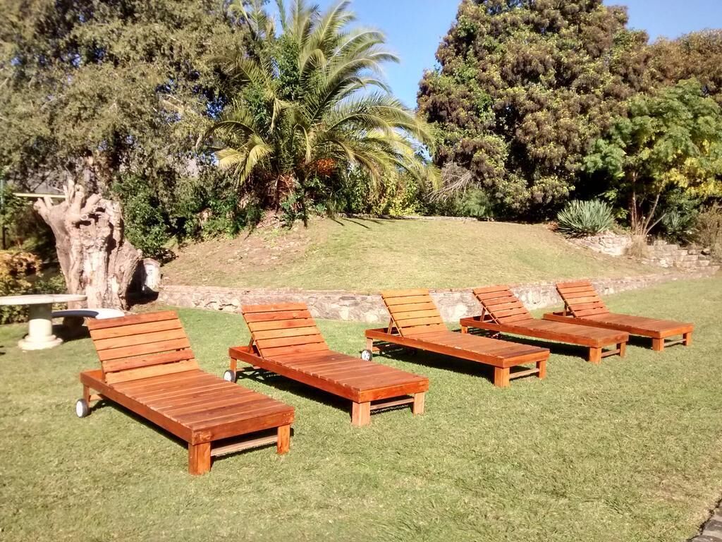 Wooden lounge chairs arranged on a grassy lawn with a backdrop of trees and a hill.