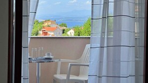A balcony with a table and a chair, overlooking a coastal town with houses and a view of the sea. - Holiday apartment with balcony and sea view (Šilo)