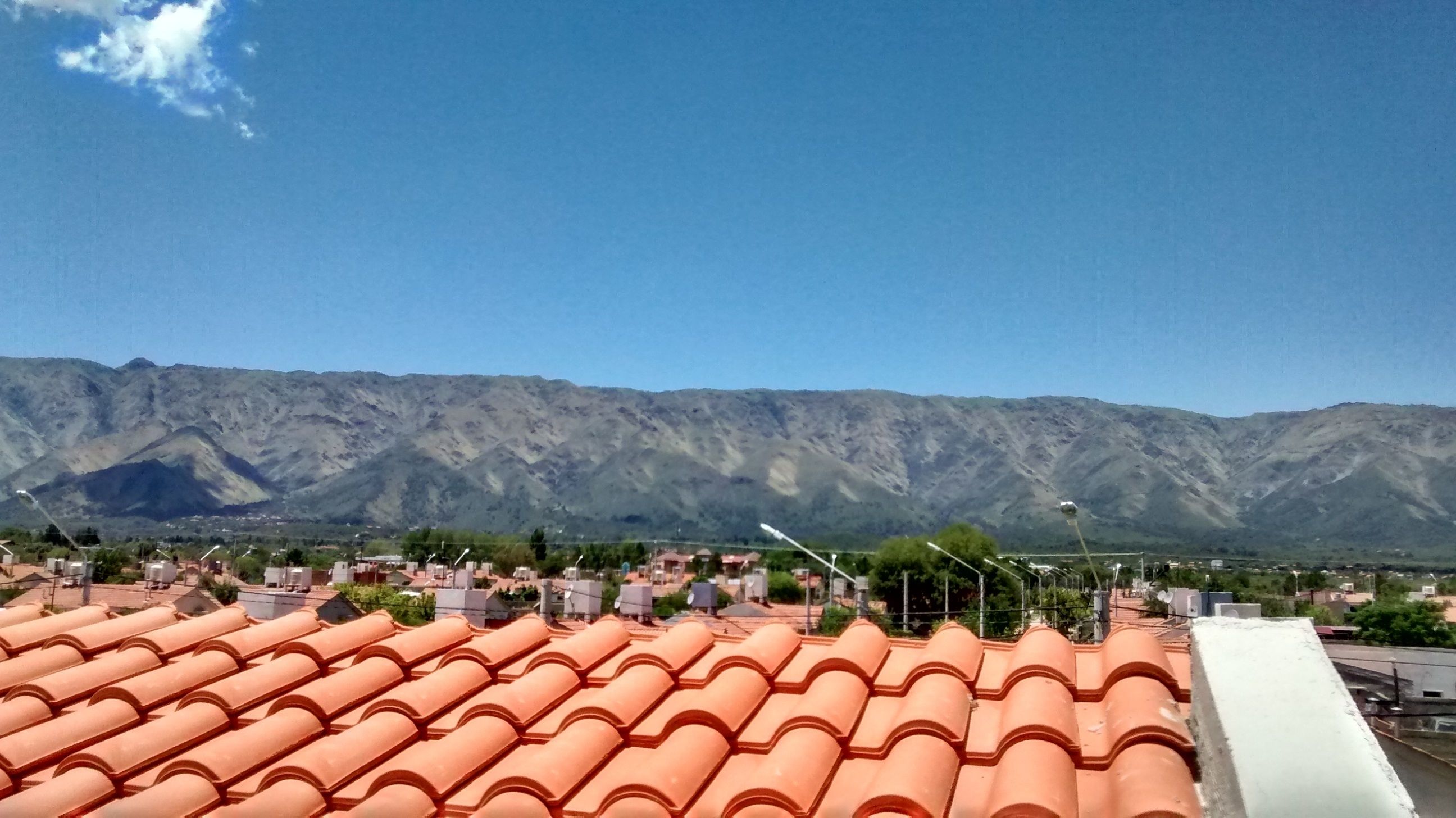 Un barrio residencial con tejados de tejas terracota, un cielo azul despejado y una cadena montañosa al fondo.