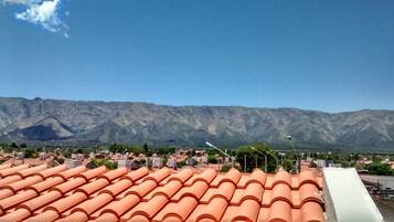 Un barrio residencial con tejados de tejas terracota, un cielo azul despejado y una cadena montañosa al fondo.