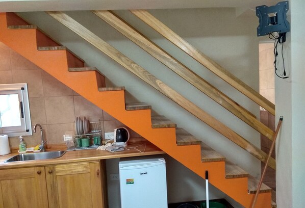 Una cocina con armarios de madera, un lavamanos, un refrigerador blanco y una escalera naranja.