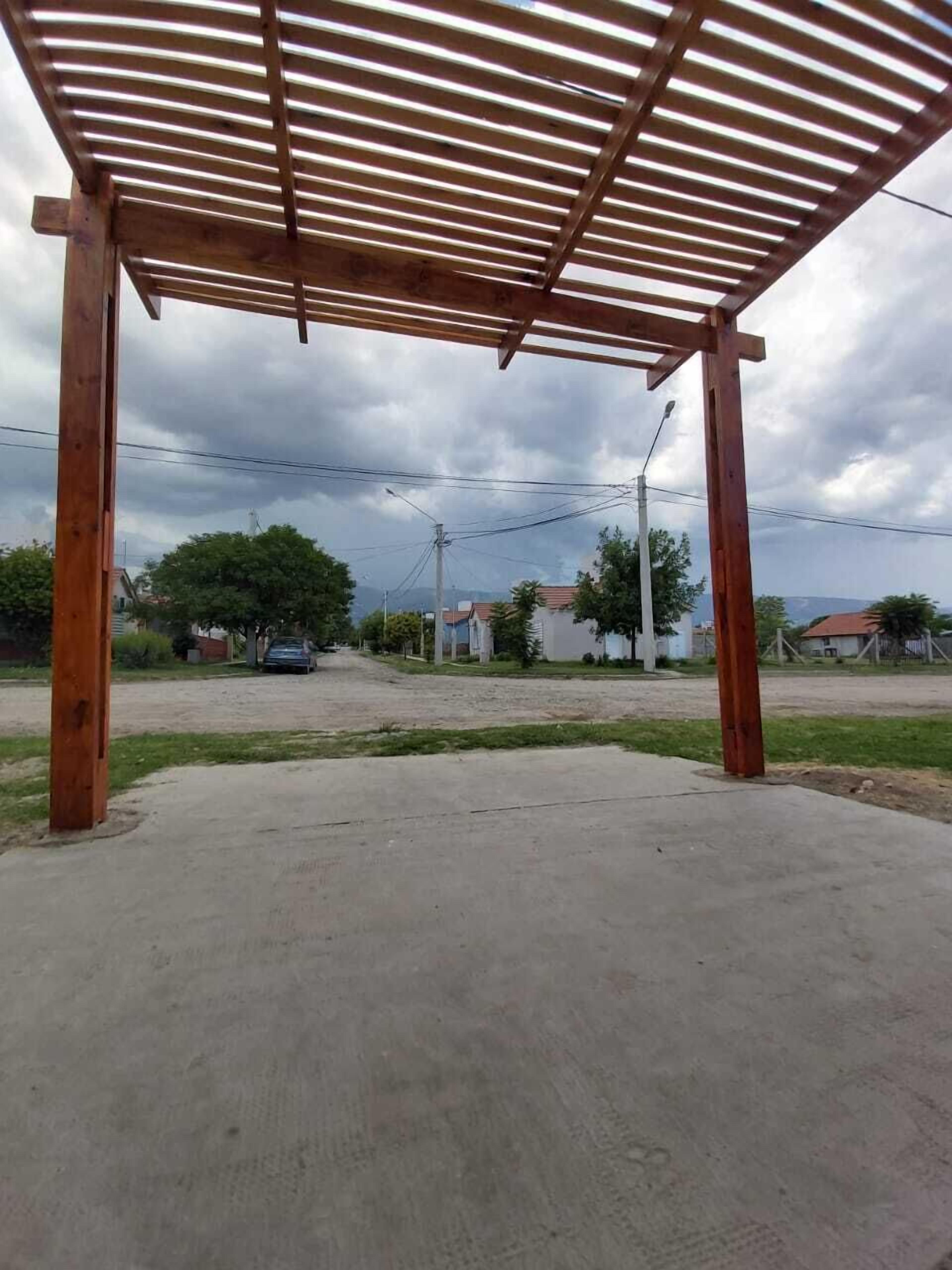 Un espacio al aire libre techado con suelo de hormigón, pilares de madera y estructura de techo metálico.