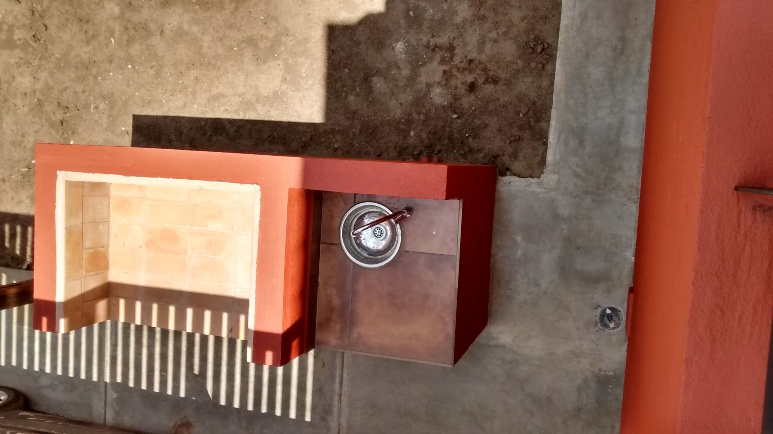 Una parrilla metálica para exteriores con un asa, adosada a una pared de hormigón.