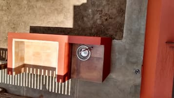 Una parrilla metálica para exteriores con un asa, adosada a una pared de hormigón.