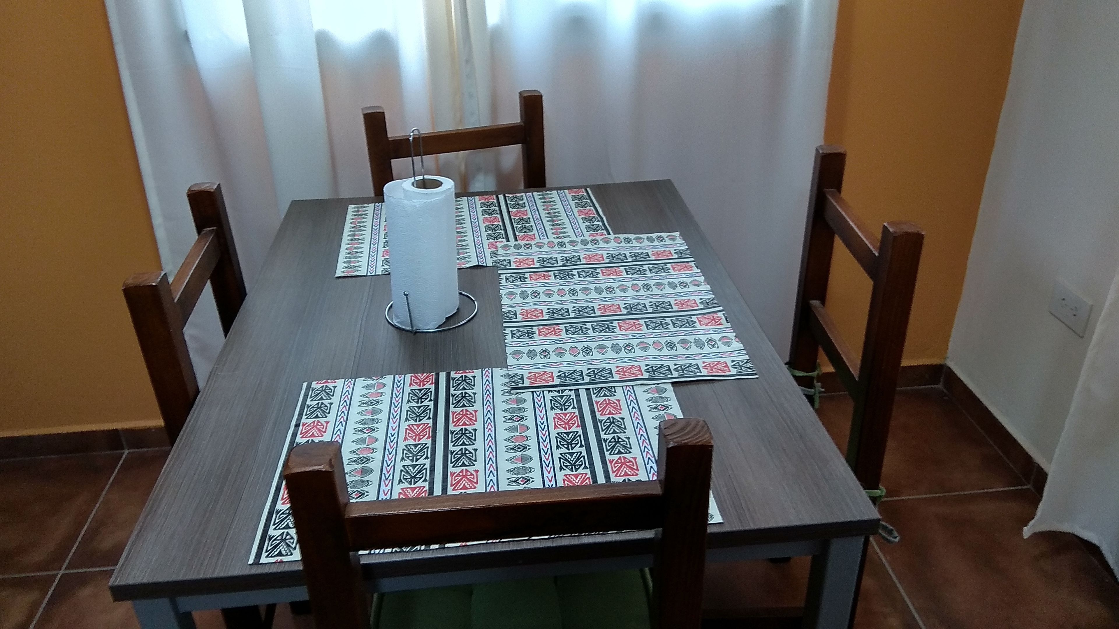 Een eettafel met een tafelkleed met patroon, een keukenroll en een groene doek.