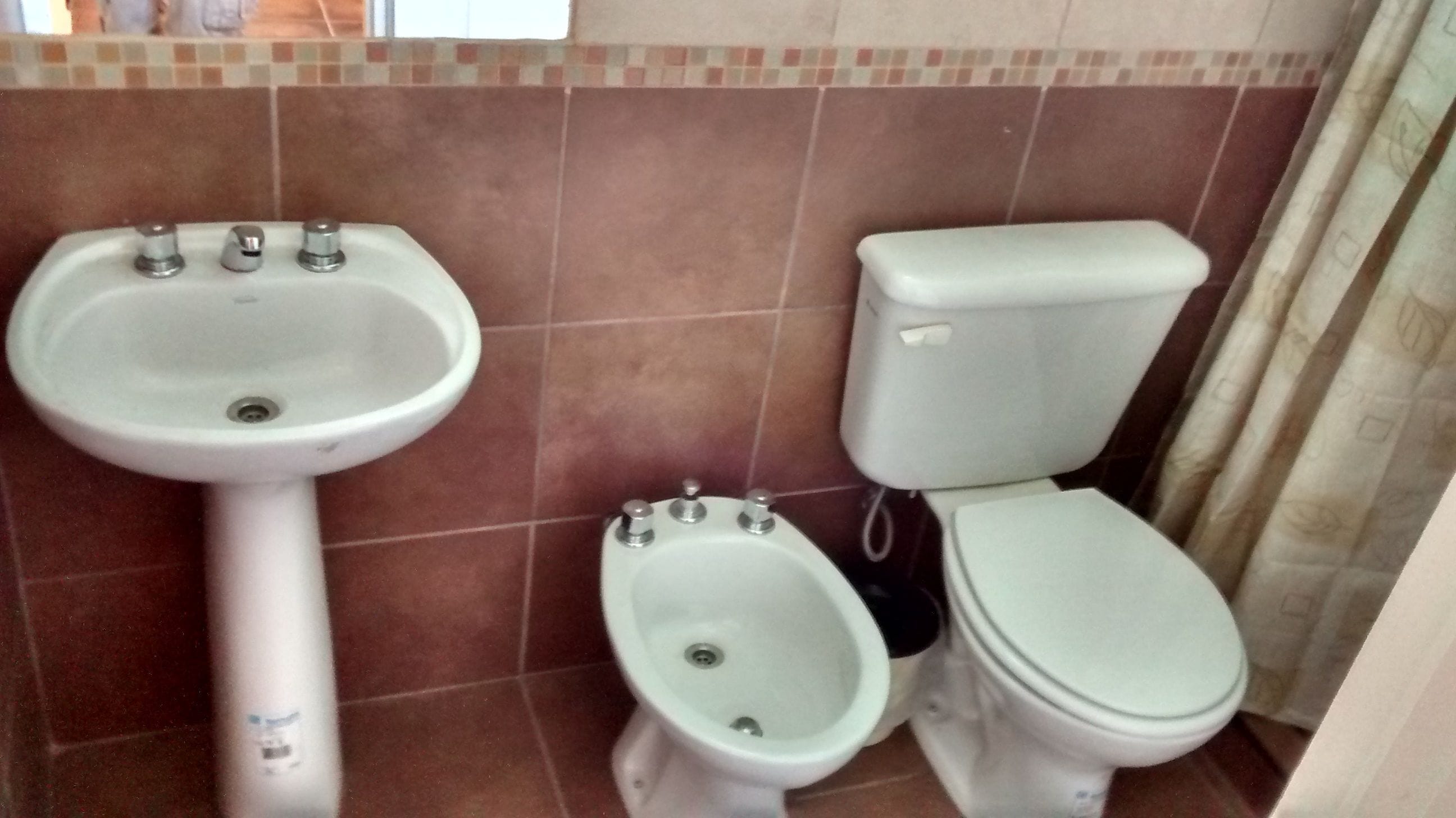 Un baño con lavamanos pedestal, un bidé y un inodoro.