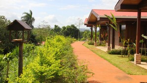 Uma trilha leva a um edifício com telhado vermelho, cercado por vegetação exuberante.