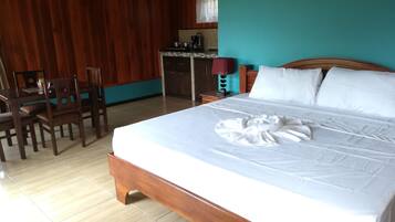 A hotel room with a wooden bed, a small kitchenette, and a dining area with chairs.