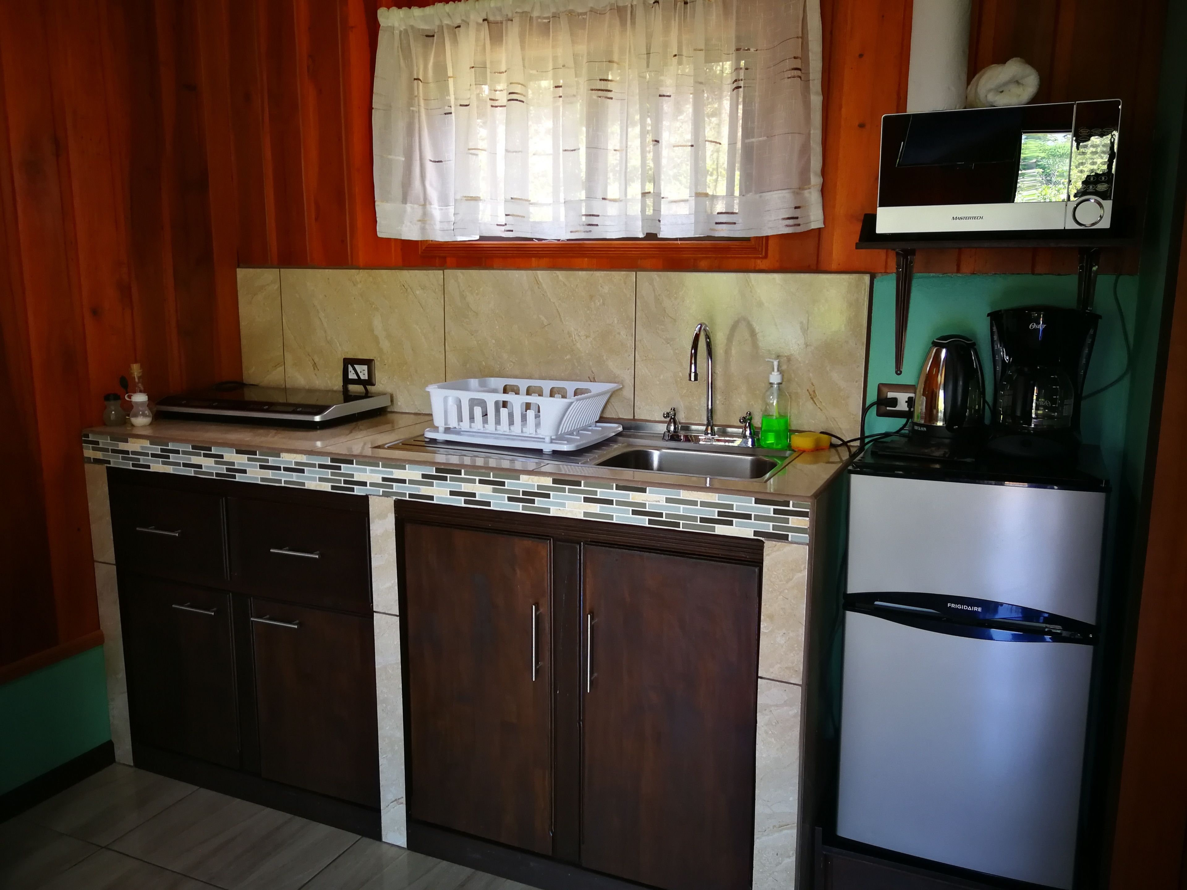 Una cocina con armarios de madera, salpicadero de azulejos, un lavamanos de acero inoxidable y un microondas.