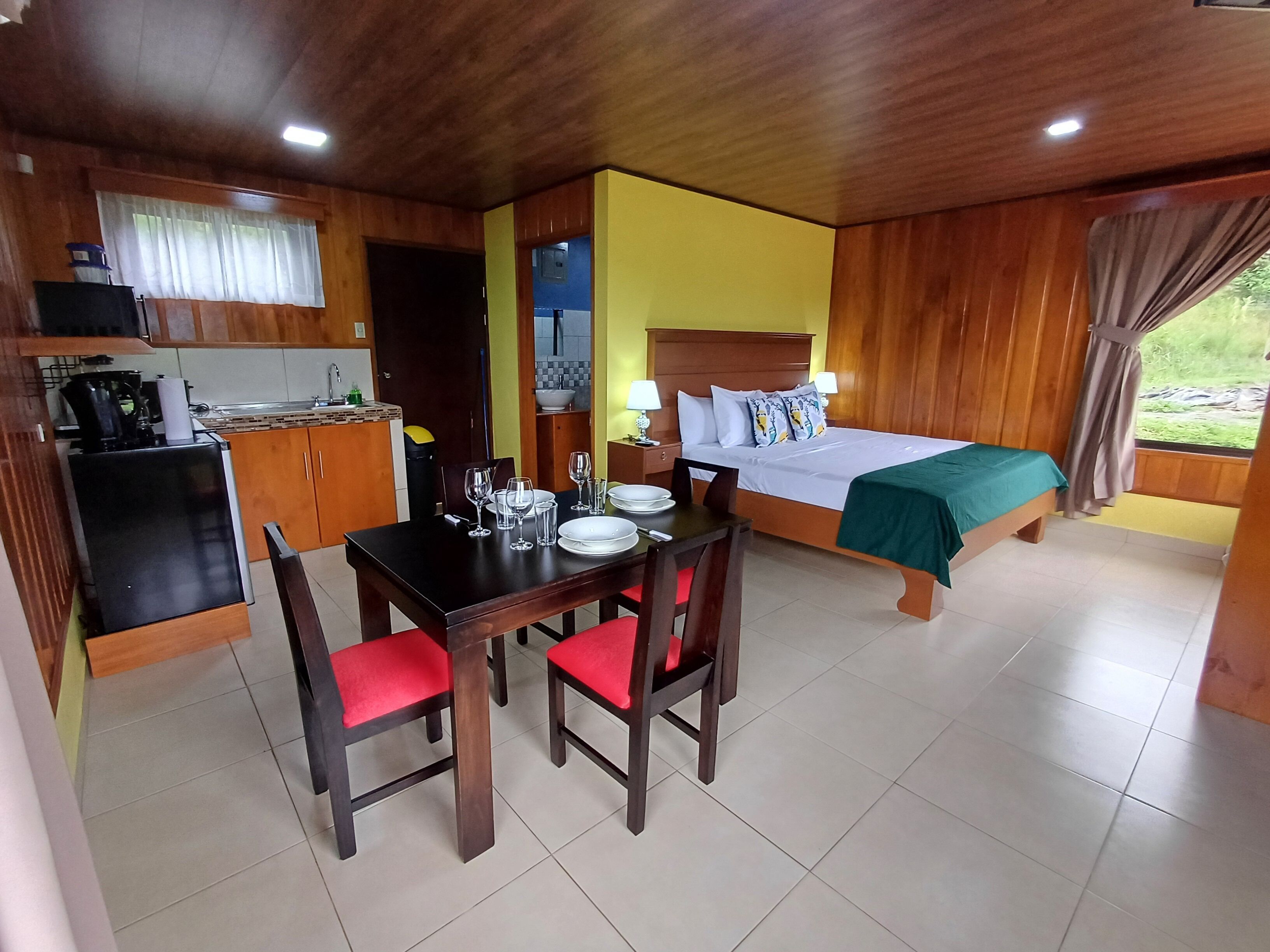 A compact hotel room with a dining area, kitchenette, and a bed with a green bedspread.