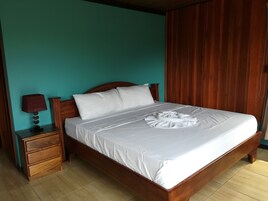 Una cama bien tendida con ropa blanca y un arreglo de toallas, una mesita de noche de madera con una lámpara y una pared color turquesa.