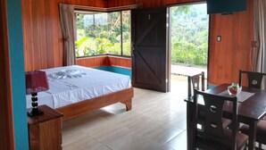 Quarto com cama, escrivaninha e vista para o verde lá fora.