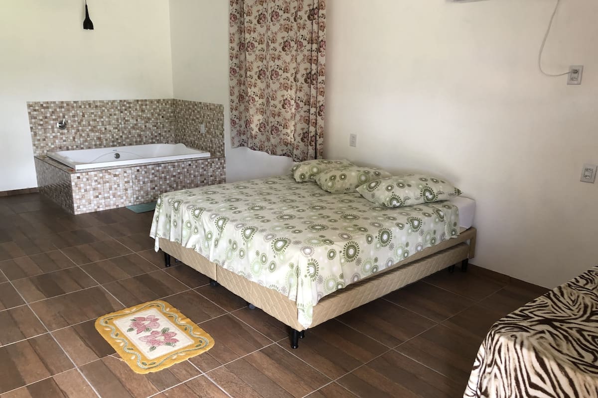 Un dormitorio con cama, un baño pequeño con bañera y un tapete estampado en el suelo.