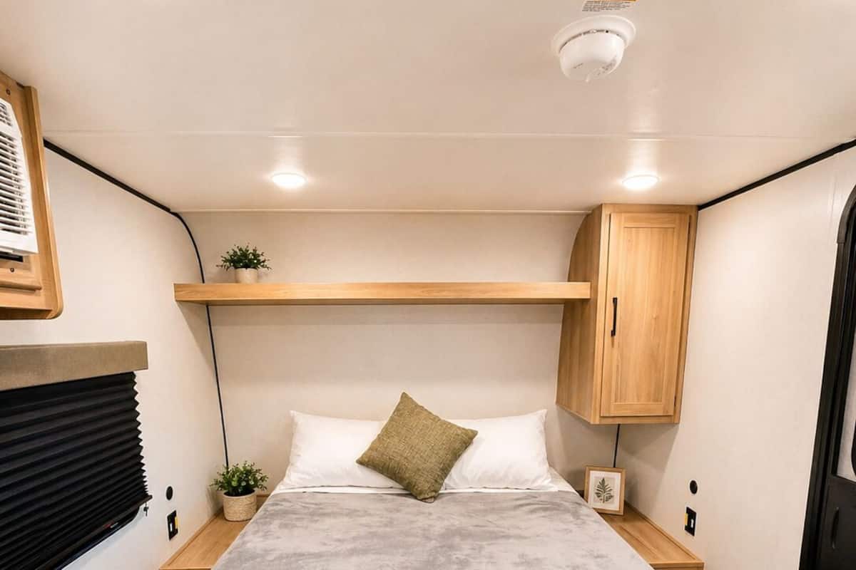 A cozy RV bedroom with a bed, bedside tables, a shelf, and a ceiling light.