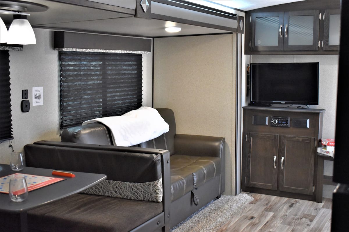 A compact RV interior with a sofa, a small table with a glass, and a television in a cabinet.