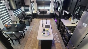 A compact kitchen with a dining area, featuring a central island, black cabinets, and a built-in oven. - Grand Canyon RV Glamping (Williams)