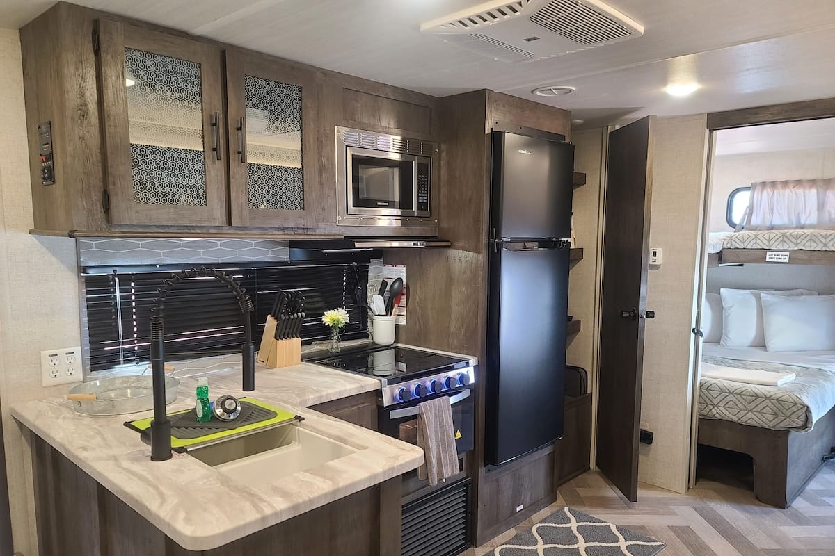 A compact kitchen with a microwave, stove, and refrigerator. A sink with a faucet and a small countertop are also visible.