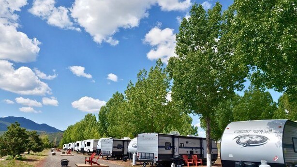 A row of RVs parked along a gravel path with trees on one side and mountains in the distance. - Grand Canyon RV Glamping (Williams)