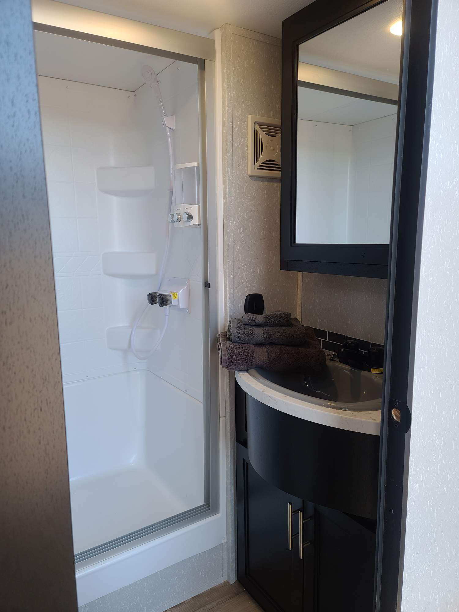A bathroom with a glass shower enclosure, a sink with a dark cabinet, and a mirror above the sink.