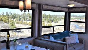 A cozy seating area with a view of a natural landscape through large windows. - Grand Canyon RV Glamping (Williams)