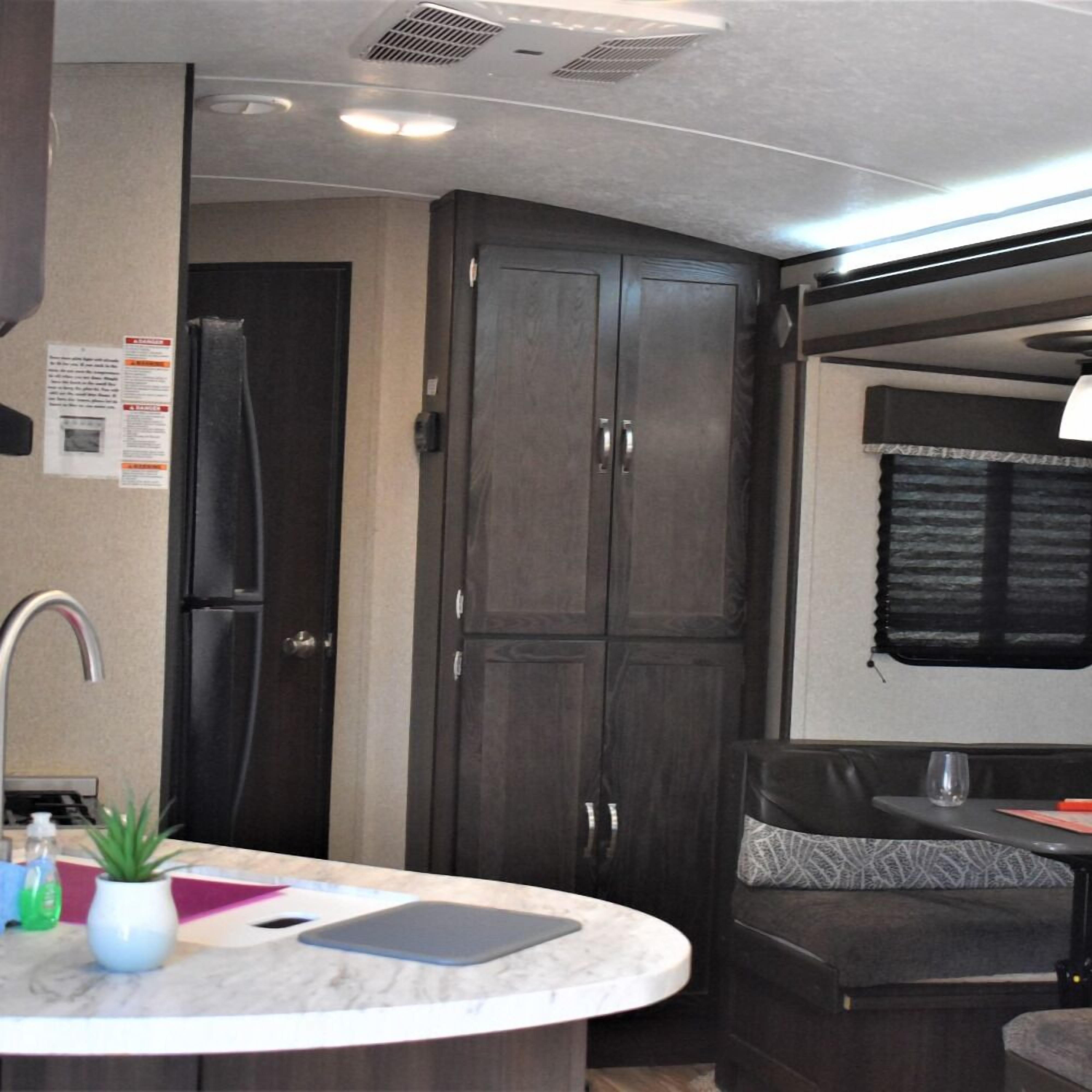 A compact RV kitchen with a sink, a refrigerator, and a dining area with a table and chairs.
