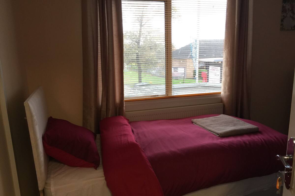 A single bed with a white headboard, a red blanket, and a beige pillow.