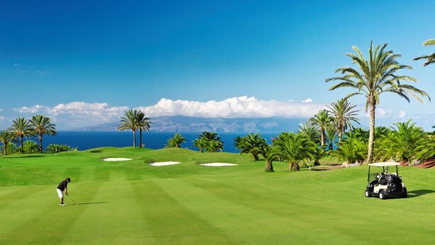 Un parcours de golf offrant une vue dégagée sur l’océan, avec des palmiers et des voiturettes de golf.