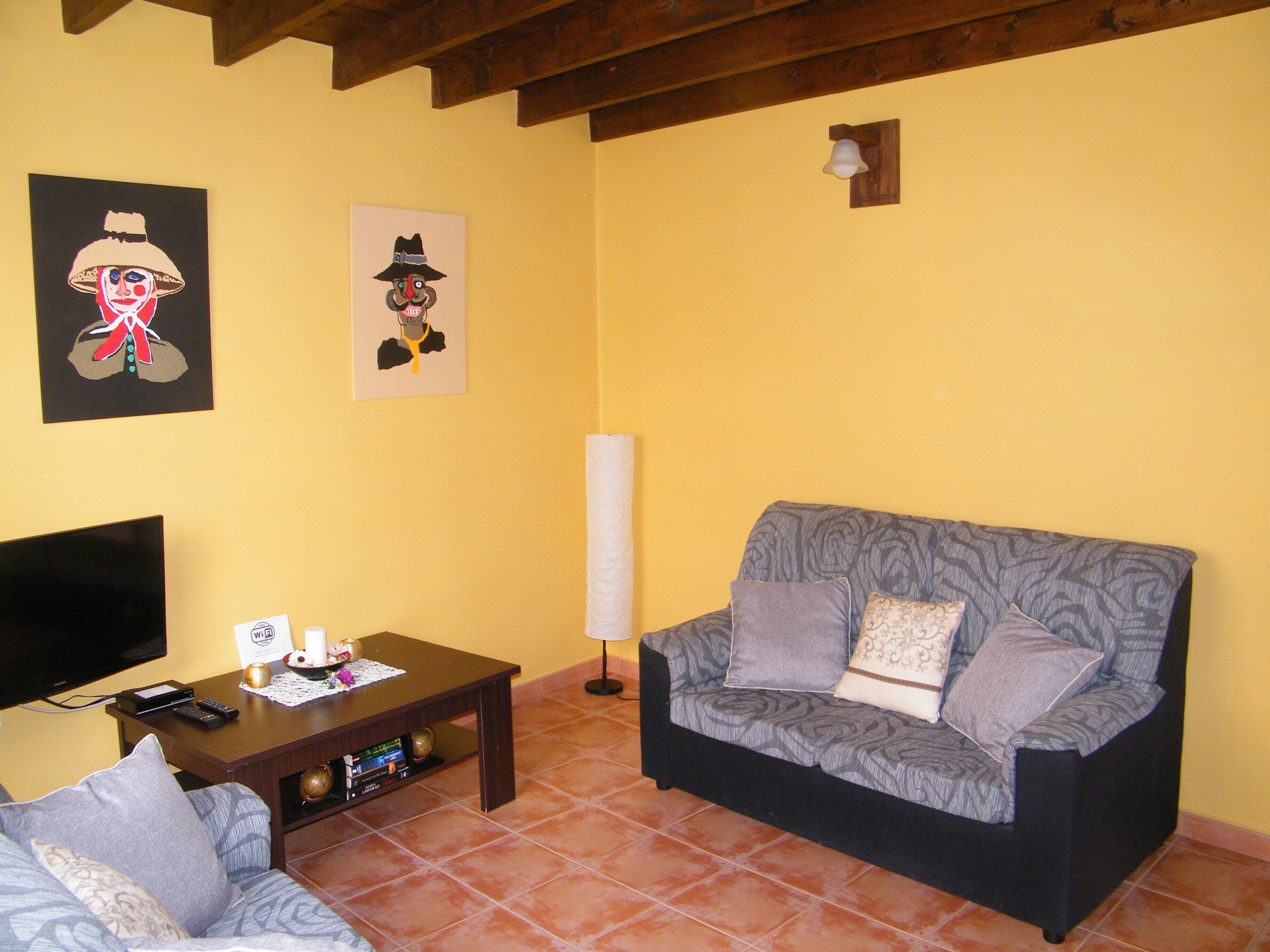 A living room with a sofa, a coffee table, a TV, and two wall-mounted artworks.