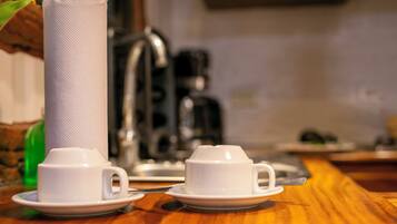 Una mesa de madera con dos tazas y platillos blancos, un rollo de papel de cocina y una cafetera.