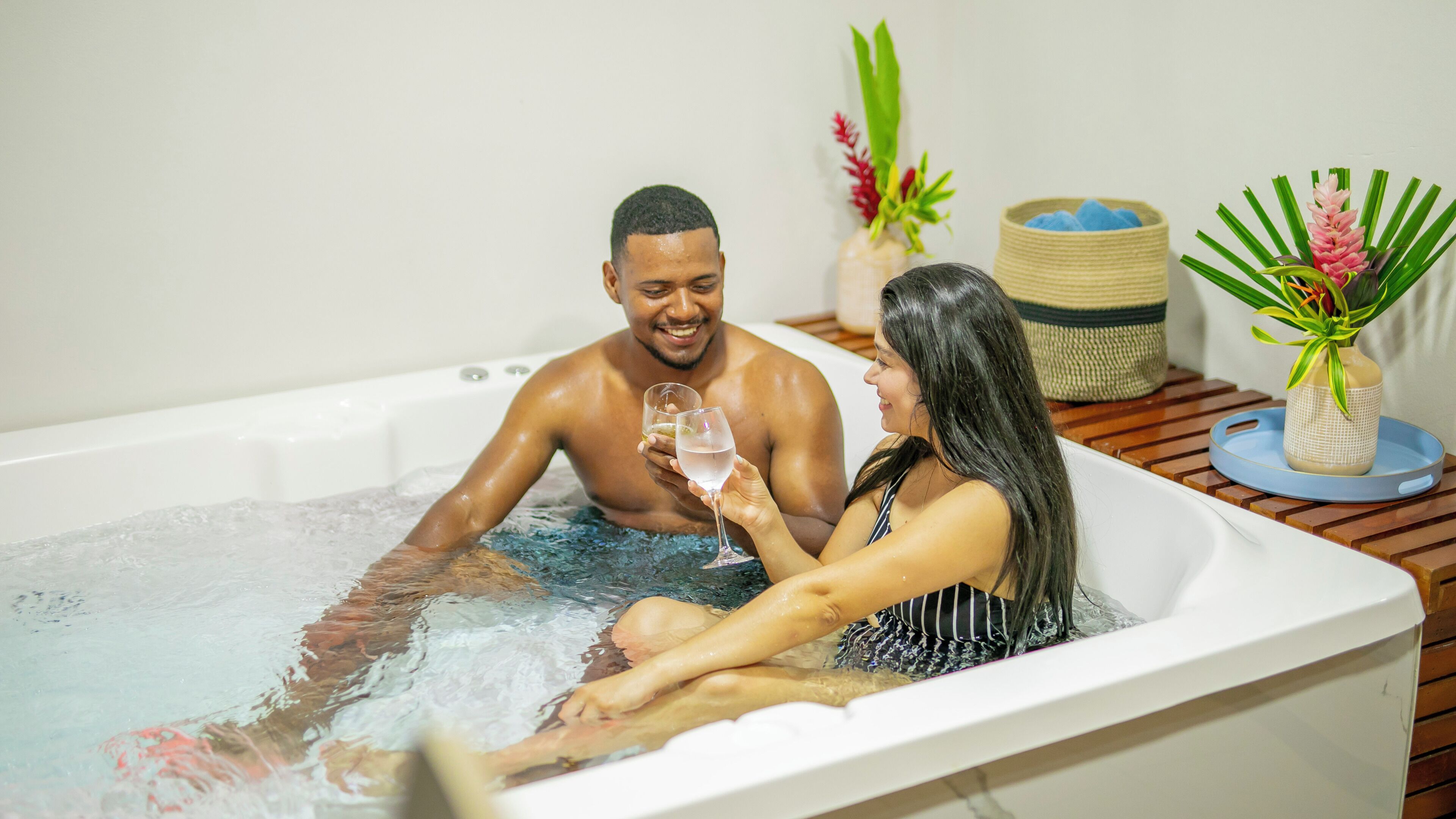 Un couple dans un bain à remous, avec une table en bois et des plantes décoratives à proximité.