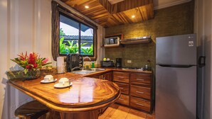 Cozinha com bancada de madeira, geladeira, micro-ondas e janela com vista para o verde.