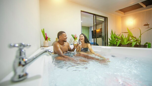 Um casal em um banheiro moderno com uma banheira, espelho e plantas em vasos.