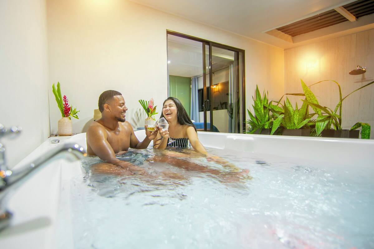 Un couple dans une salle de bain moderne, avec une baignoire, un miroir et des plantes en pot.