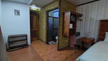 Un dormitorio con cama, armario de madera, mesita de noche con lámpara y puerta que da a un baño.