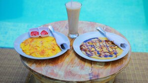 Two plates of food and a drink on a round table by a pool. - The Box House Nusa Penida (Penida Island)
