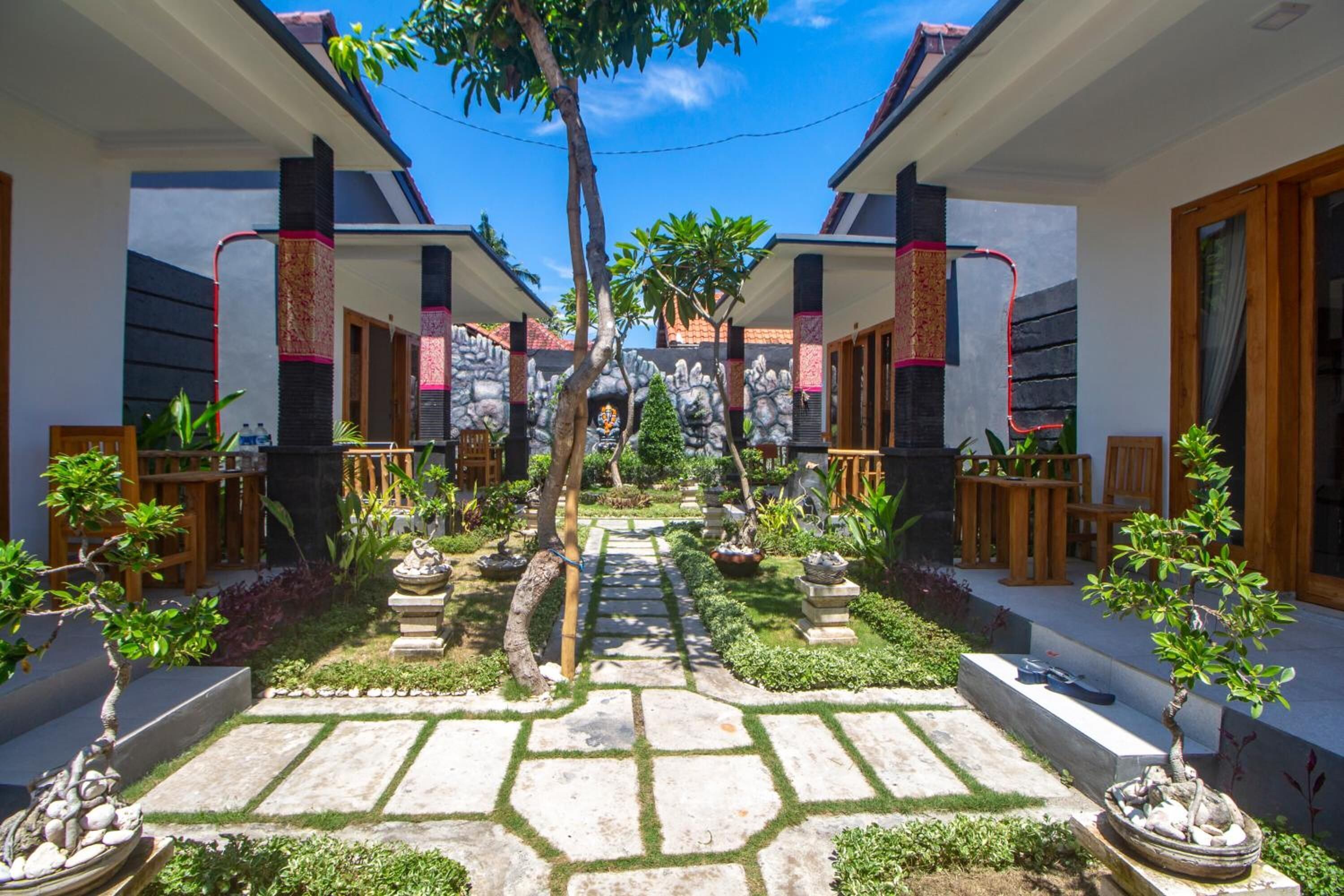 A courtyard with a stone pathway, potted plants, and a central statue.