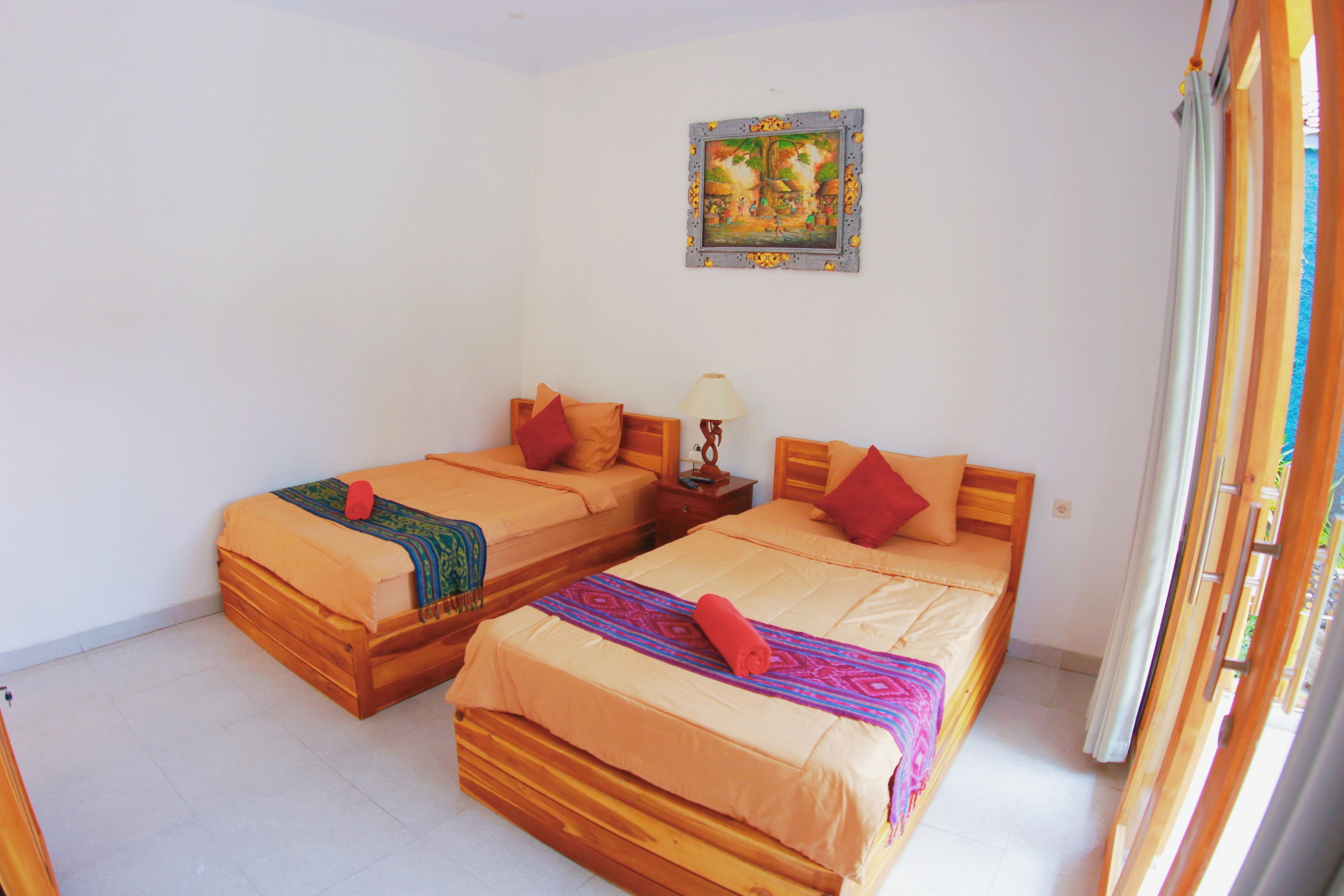 A room with two wooden beds, each with a pillow and a blanket. There is a painting on the wall and a window with curtains.