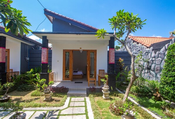 A two-story house with a covered porch, a stone wall, and a garden with various plants and a stone pathway.