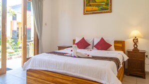 A bedroom with a wooden bed, two red pillows, a white duvet, a painting on the wall, and a nightstand with a lamp. - The Box House Nusa Penida (Penida Island)