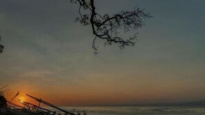 A beach scene with a sunset, a pier, and boats. - The Box House Nusa Penida (Penida Island)