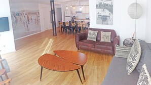 A spacious living area with a wooden coffee table, a red sofa with patterned cushions, and a grey sofa with decorative pillows. A dining area with a wooden table and chairs is visible in the background. - Design, quality, tranquility, and very central (Alicante)