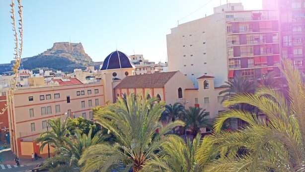 A coastal cityscape with a prominent hill in the background, a building with a dome, and palm trees in the foreground. - Design, quality, tranquility, and very central (Alicante)